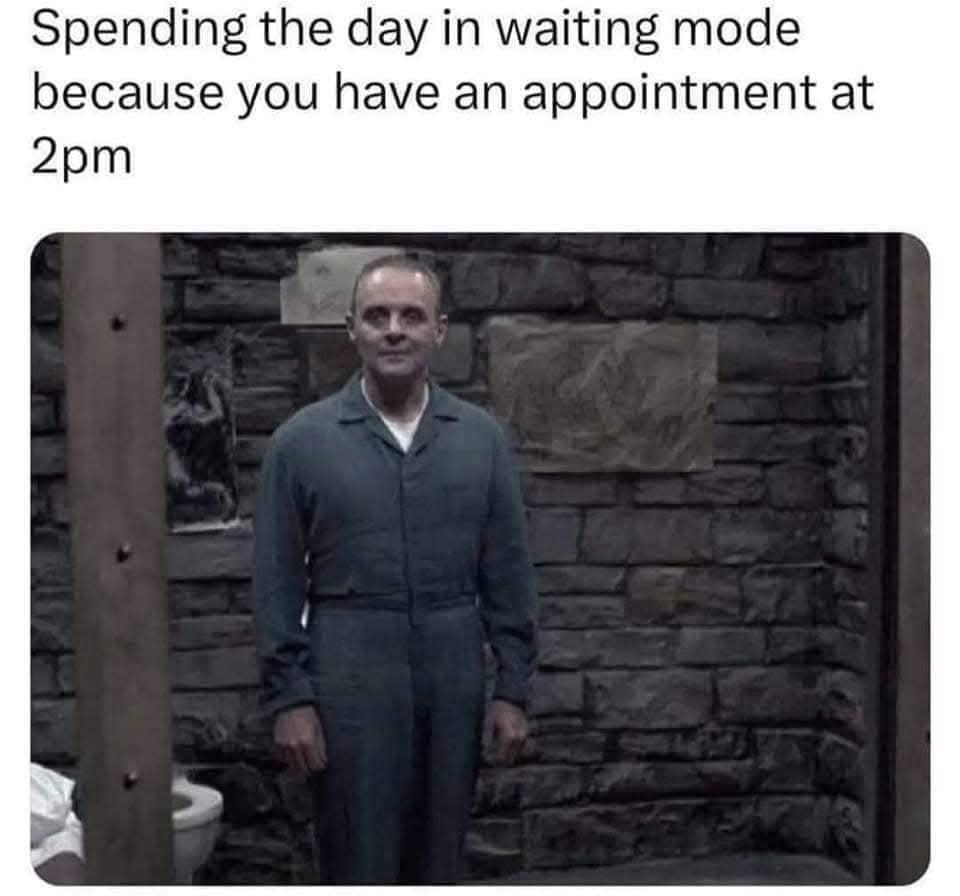 Man in gray jumpsuit stands in stone-walled room; caption jokes about waiting for a 2pm appointment