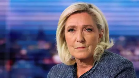 Reuters Headshot of Le Pen, on the right-hand side of the screen, staring into the camera