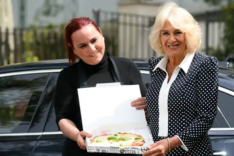 Getty Images Queen Camilla, wearing a polka dot collared dress, receives a margherita pizza in a takeaway box in Rome