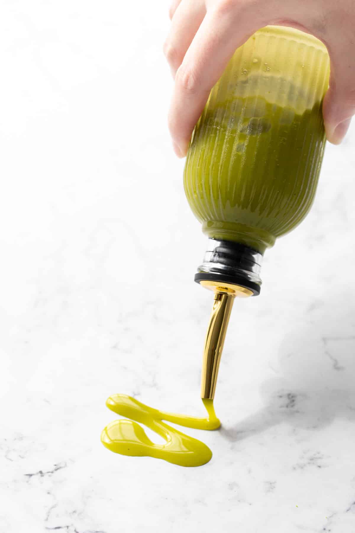 Drizzle of bright green pistachio syrup on a marble background.