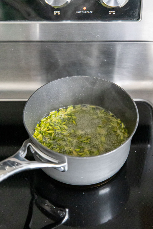 Small saucepan with boiling sugar syrup and green slivered pistachios on the stovetop.