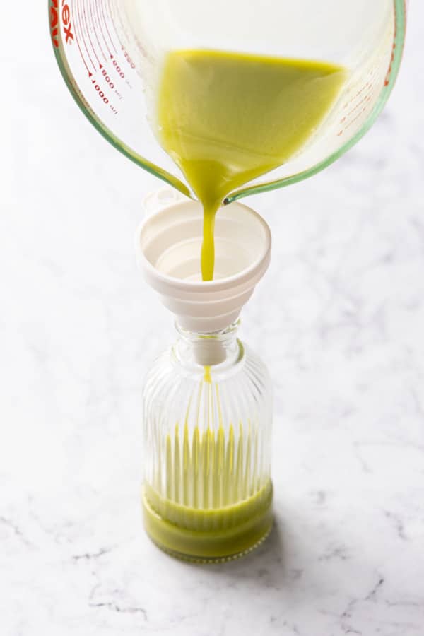 Pouring pistachio syrup through a funnel into a decorative glass jar.