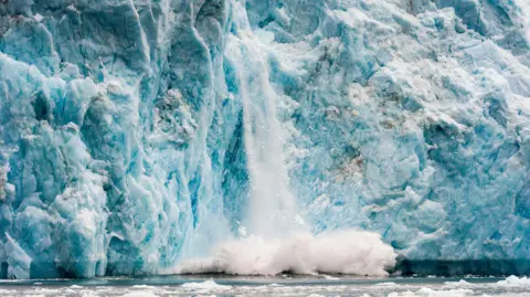 Getty Ice falling from blue, crevassed ice cliff into the ocean where it makes a splash