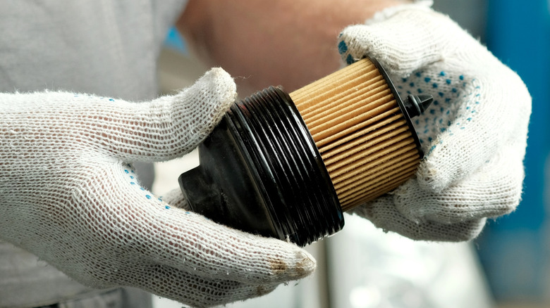 A person with gloves handling a plastic oil filter canister