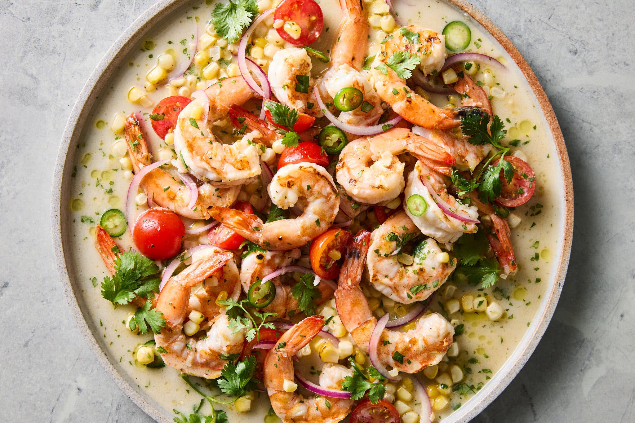 An overhead image of shrimp tossed with a citrusy sauce, corn and jalapeño.