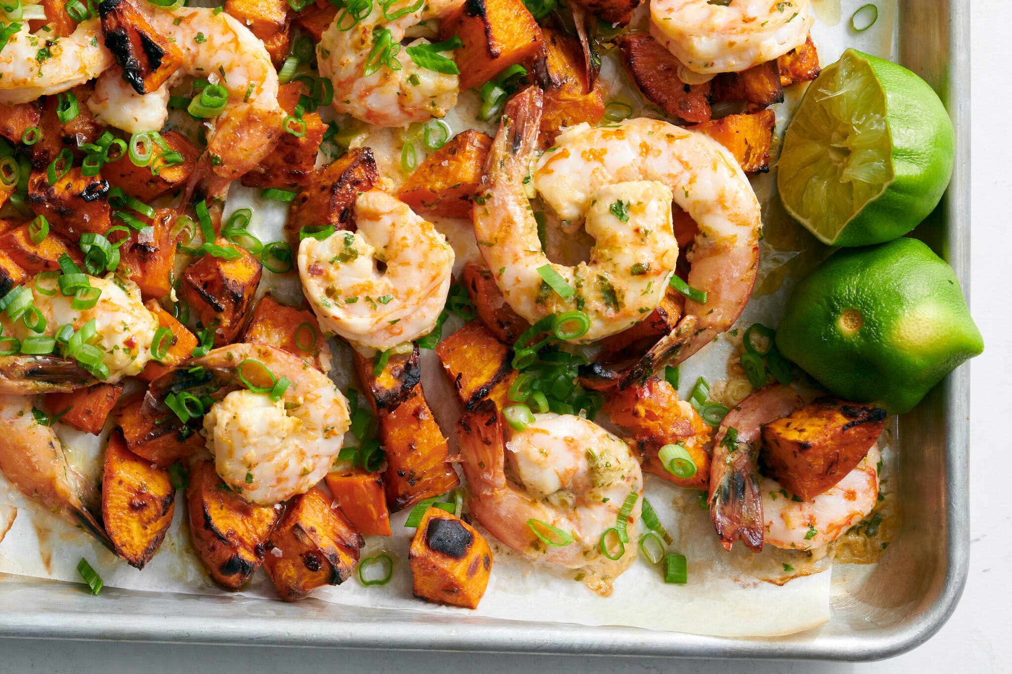 An overhead image of shrimp and sweet potatoes on a rimmed sheet pan next to spent lime halves.
