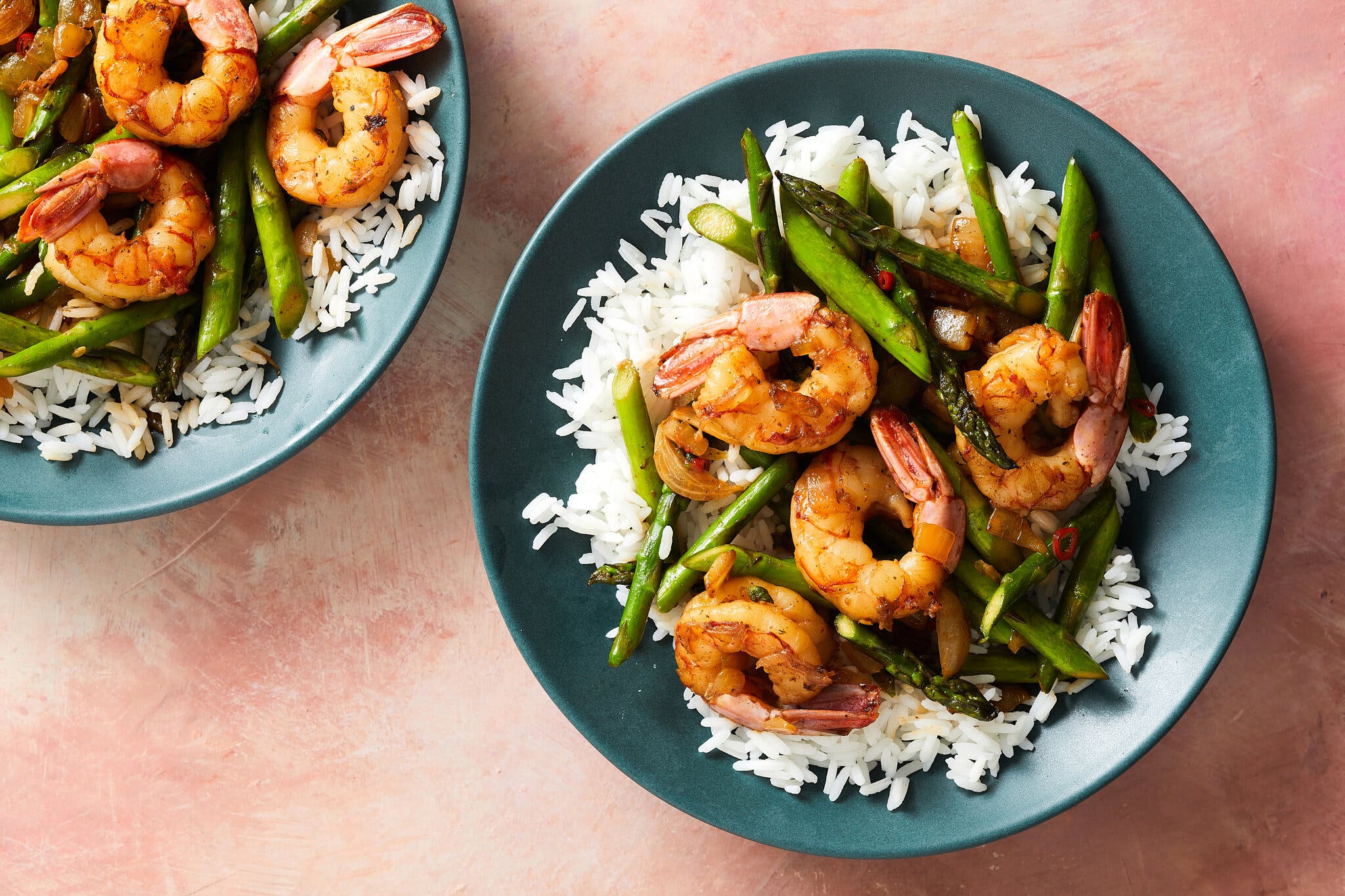 Two teal bowls are filled with white rice topped with golden shrimp and short pieces of asparagus.
