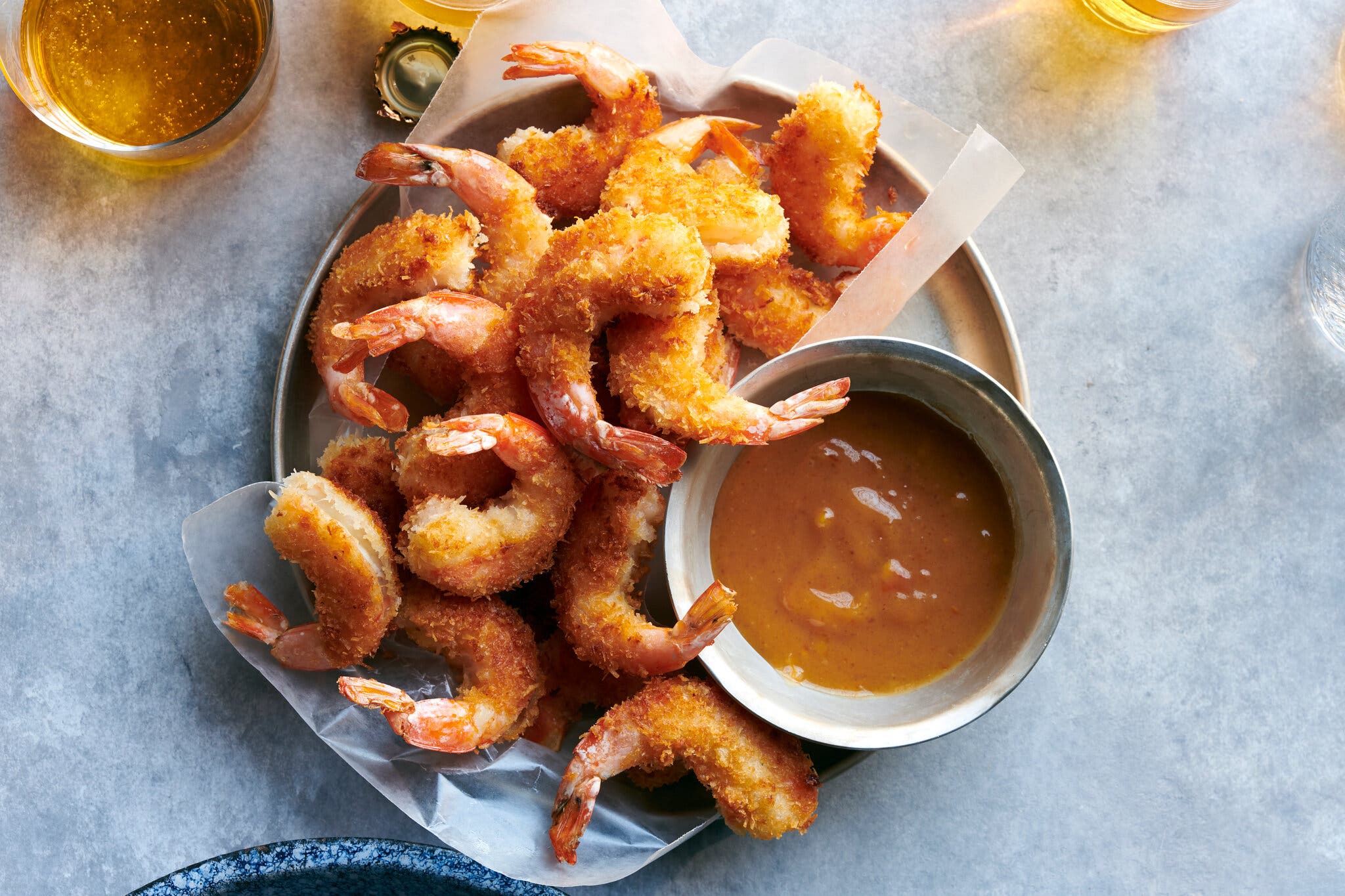 A round tin is filled with fried golden brown shrimp and a bowl of dipping sauce.