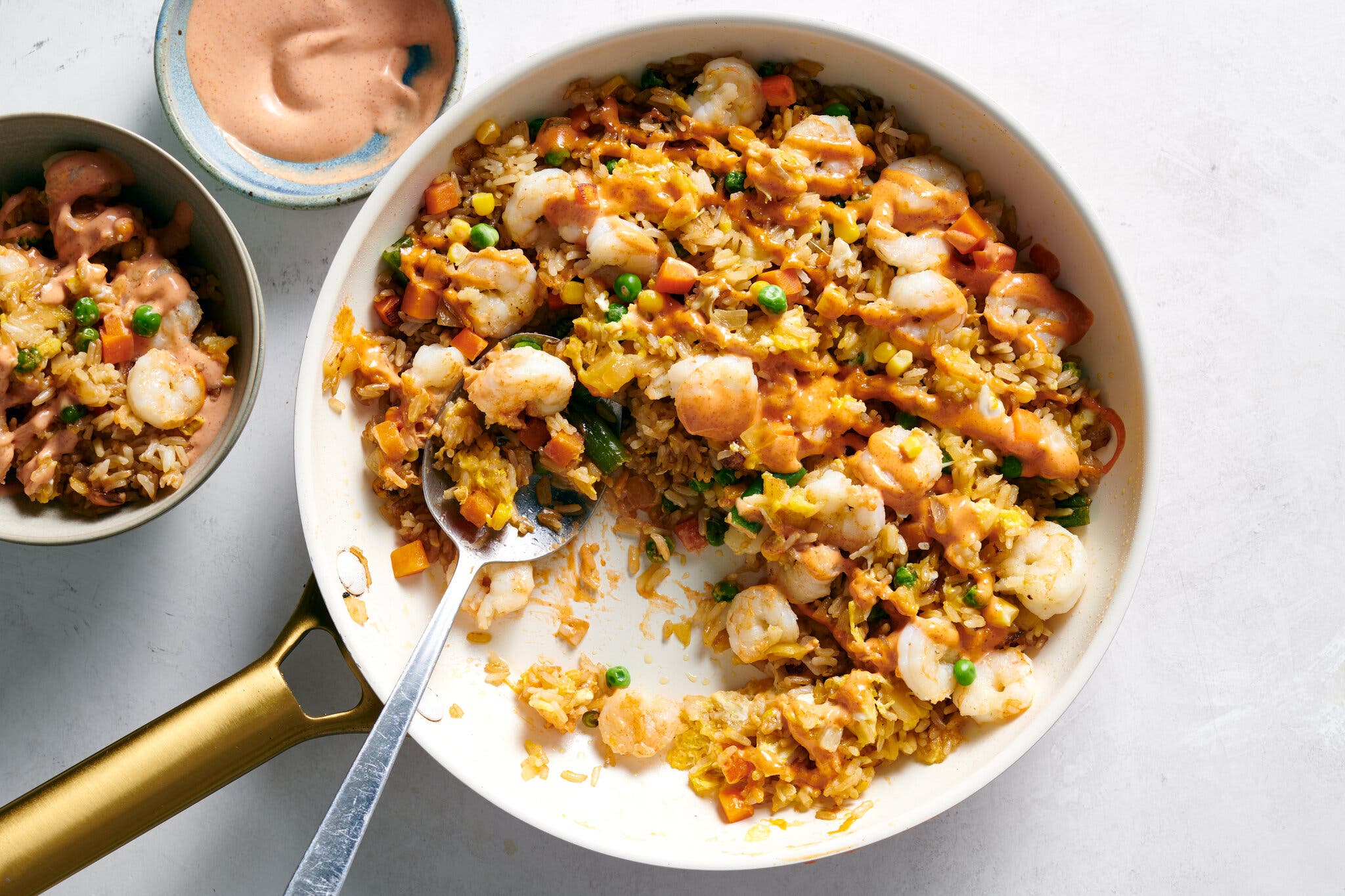 A white skillet with a gold handle holds shrimp fried rice next to a bowl of the rice.