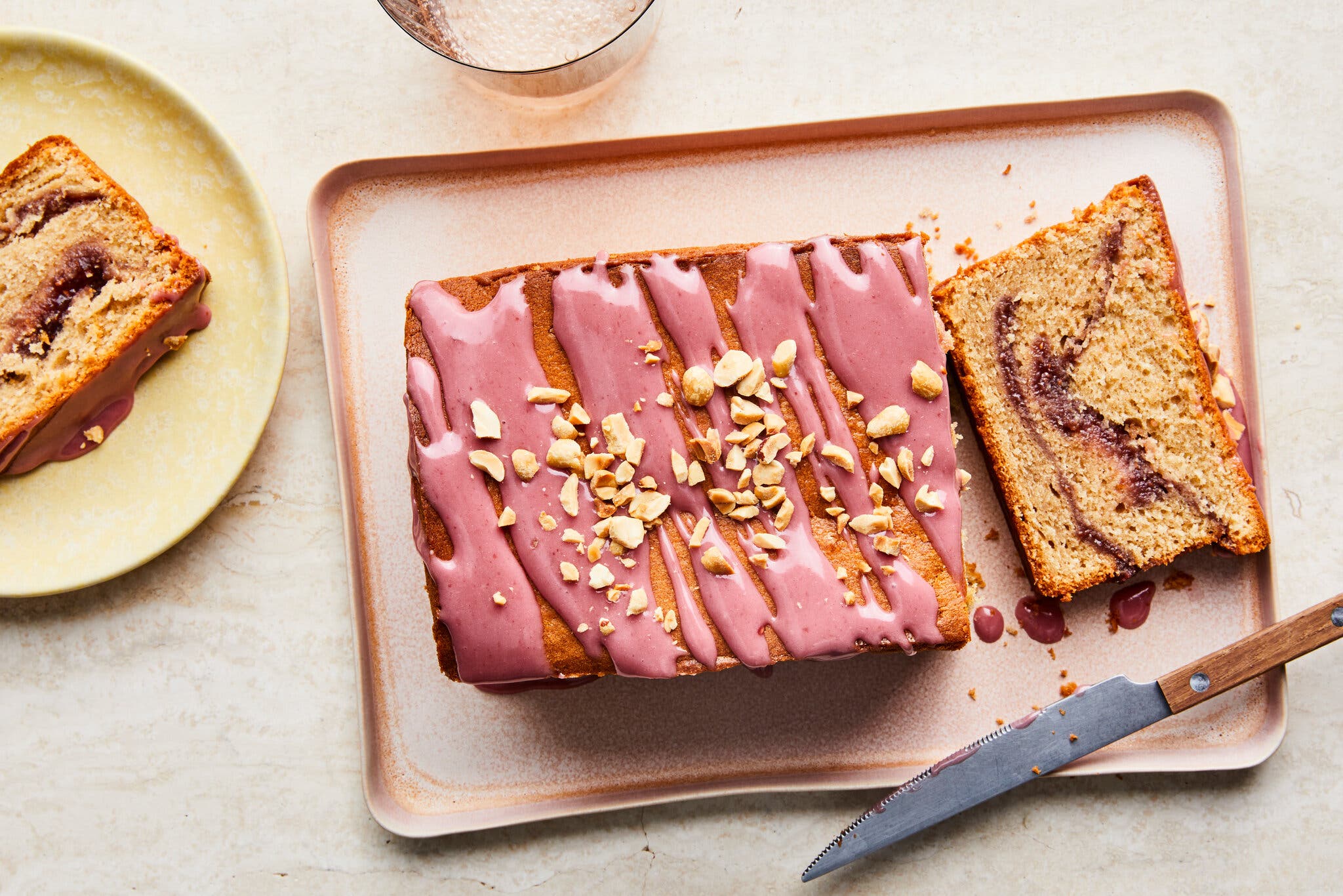 A swirled loaf finished with a light purple glaze is photographed from overhead on a platter. It’s partly sliced, with one slice sitting off to the side.