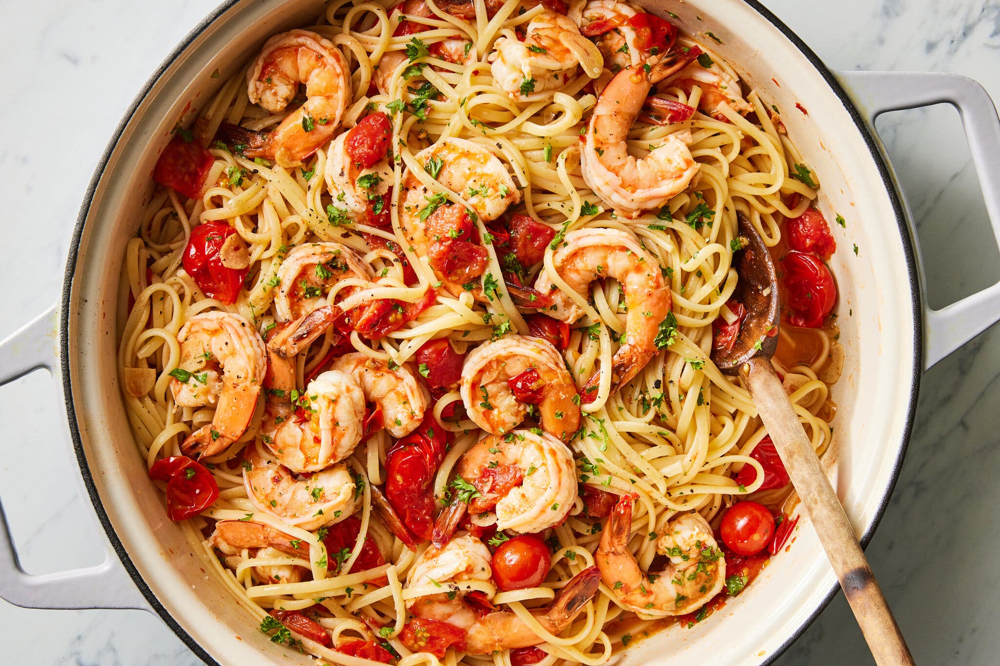 A white handled pan is filled with spaghetti, shrimp and burst cherry tomatoes.