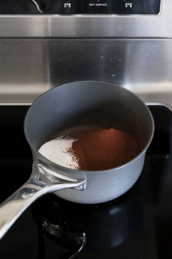 Small saucepan with sugar and cocoa powder on a stovetop.