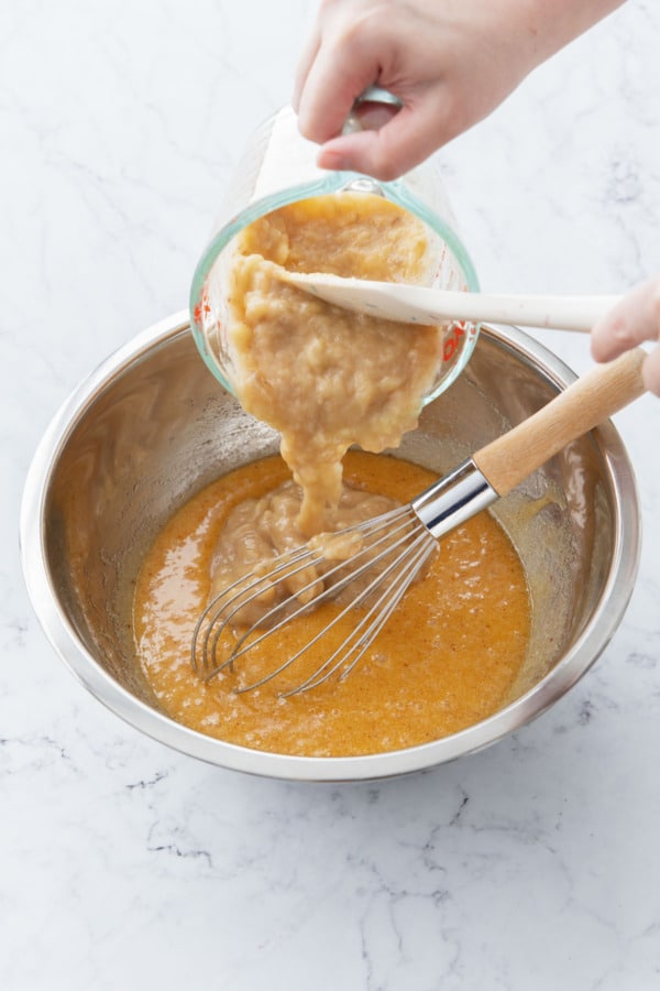Adding mashed banana to mixing bowl with other ingredients.