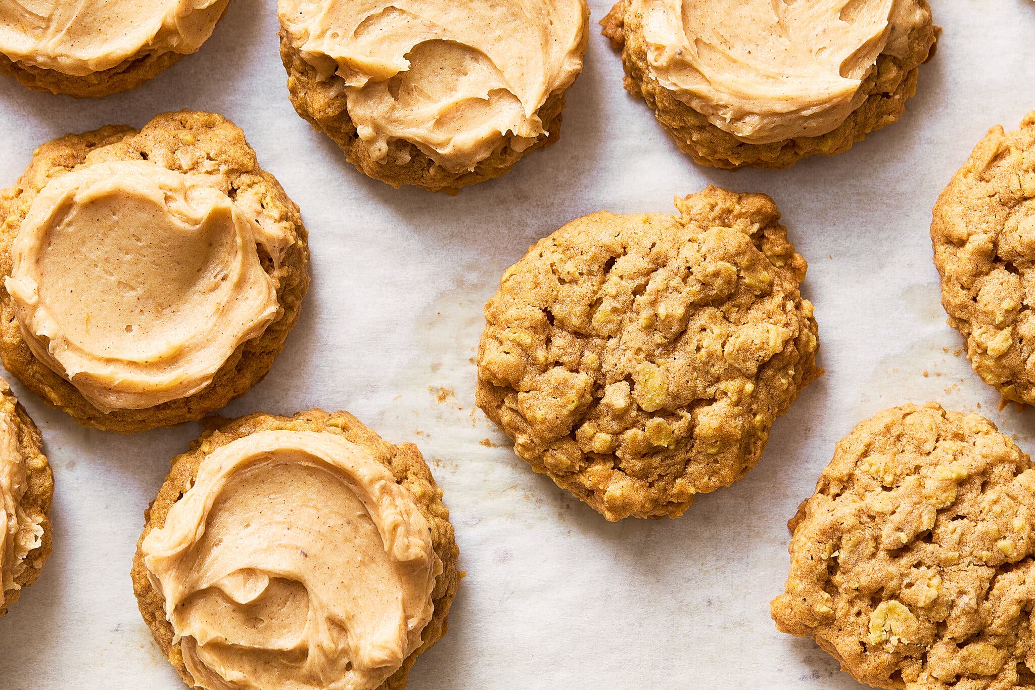 A close-up of several pumpkin cookies with a light-colored frosting on top, arranged on a white surface.
