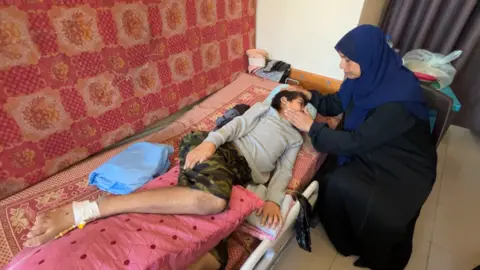 Amar Abu Said, a Palestinian boy, lies on a bed, looking poorly, as a woman touches his face