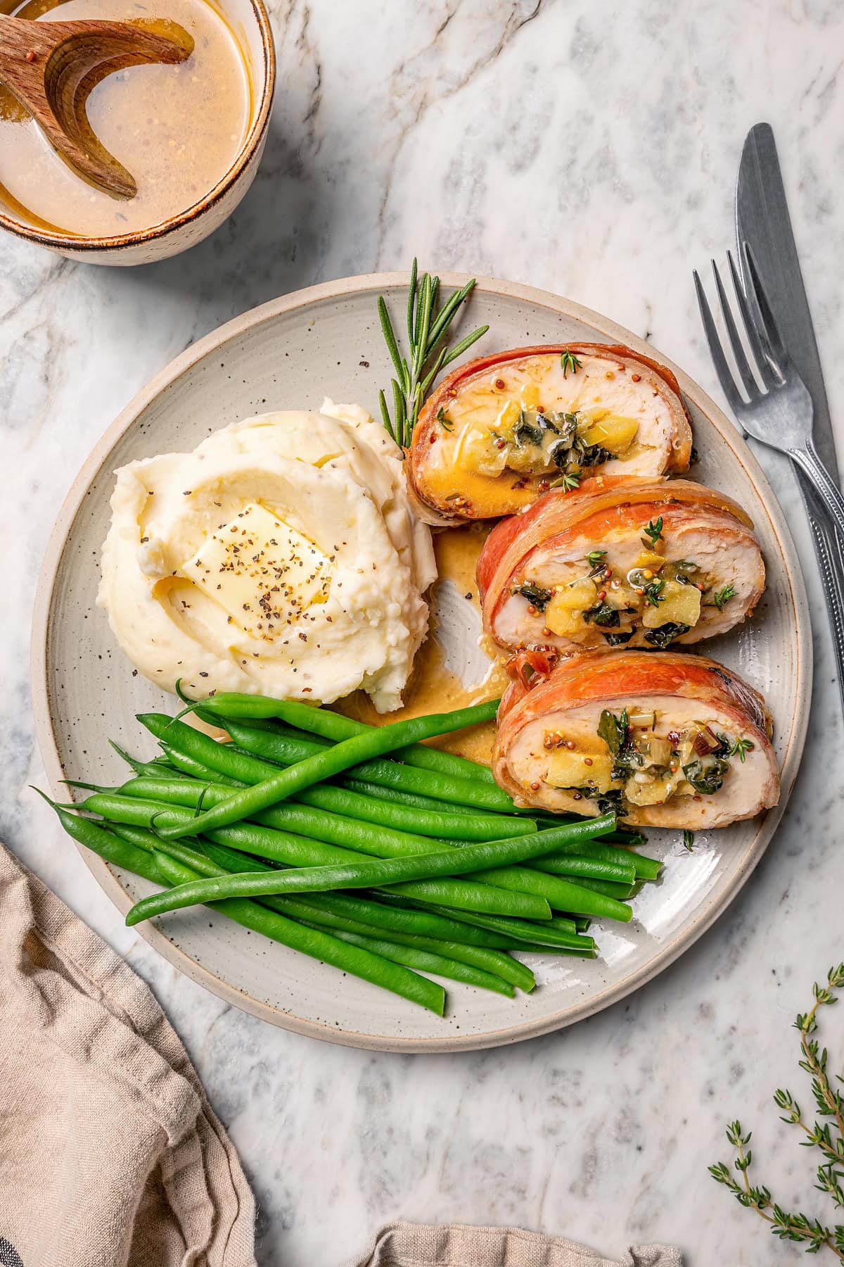 This Prosciutto Wrapped Stuffed Turkey Tenderloin recipe is filled with apples, cheese and kale for a healthy high-protein dinner. Delicious! Plate of prosciutto-wrapped stuffed turkey tenderloin, green beans, and mashed potatoes.