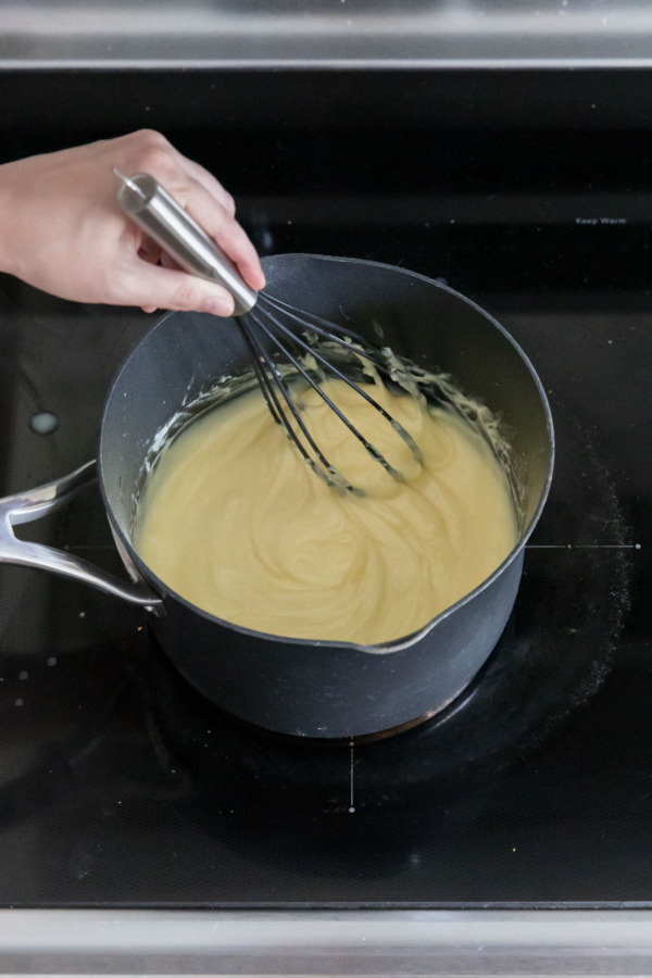 Cooking the custard until it thickens to a pudding-like consistency, whisking regularly.