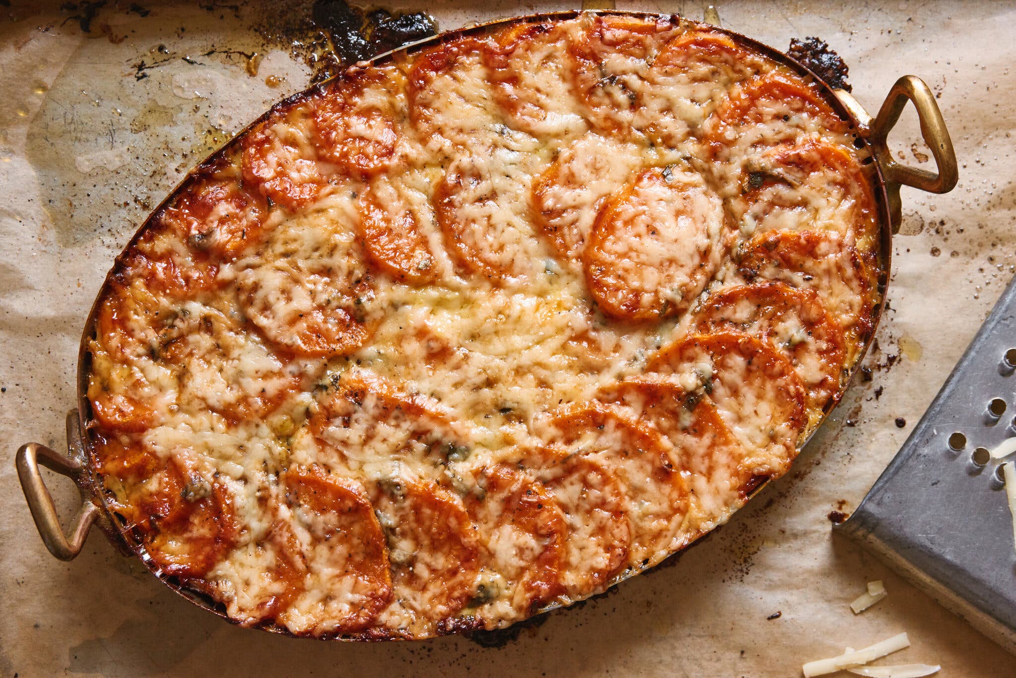 An oval baking dish filled with slices of sweet potato topped with gooey melted cheese.