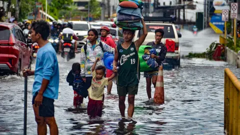 AFP via Getty Images Residents carrying their belongings, wade through a flooded street in Mandaue City, Cebu province 