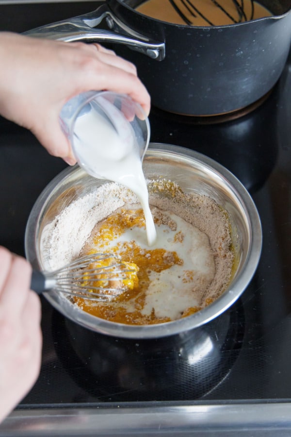 Whisking 1/4 cup of milk into the bowl with the egg yolks.
