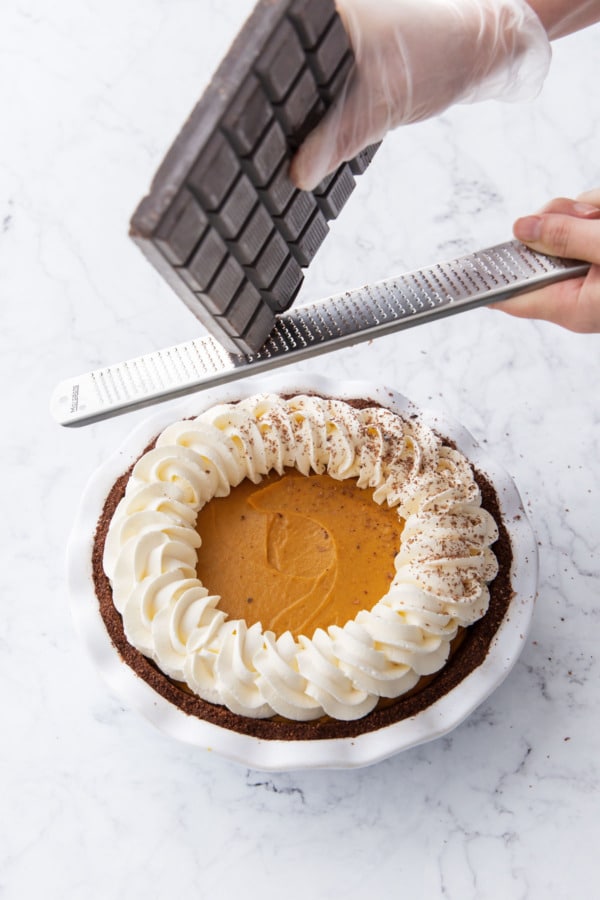 Decorating the finished pie by grating chocolate on top with a microplane grater.
