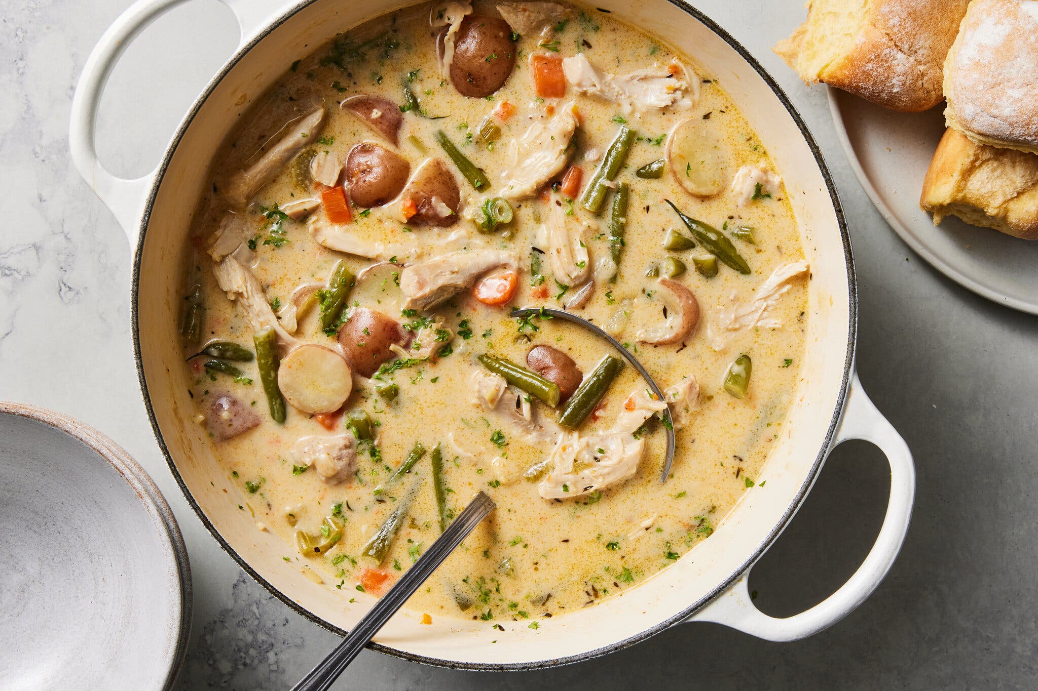 An overhead image of a white Dutch oven filled with soup studded with chicken, potatoes and green beans.
