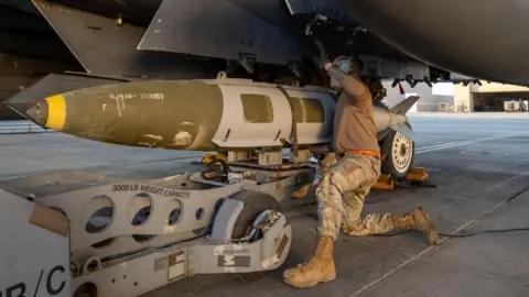 Reuters A US airman attaches a munitions system to an F-15 fighter jet taking part in Operation Hawkeye Strike. Photo: 19 December 2025