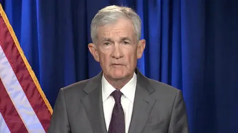 Reuters US Fed chair Jerome Powell stands in front of a blue curtain and US flag. 